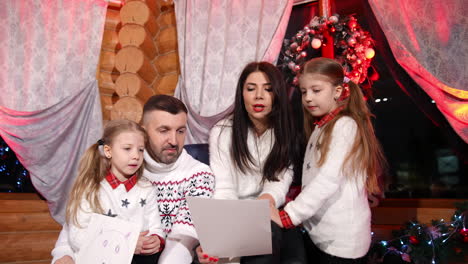 young family sit together in the living-room at christmas. mother reading a letter to santa and her husband and little girls listen. positive festive atmosphere at home.