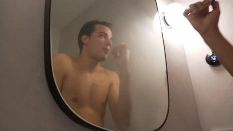 man brushing his teeth in front of the mirror after taking a bath