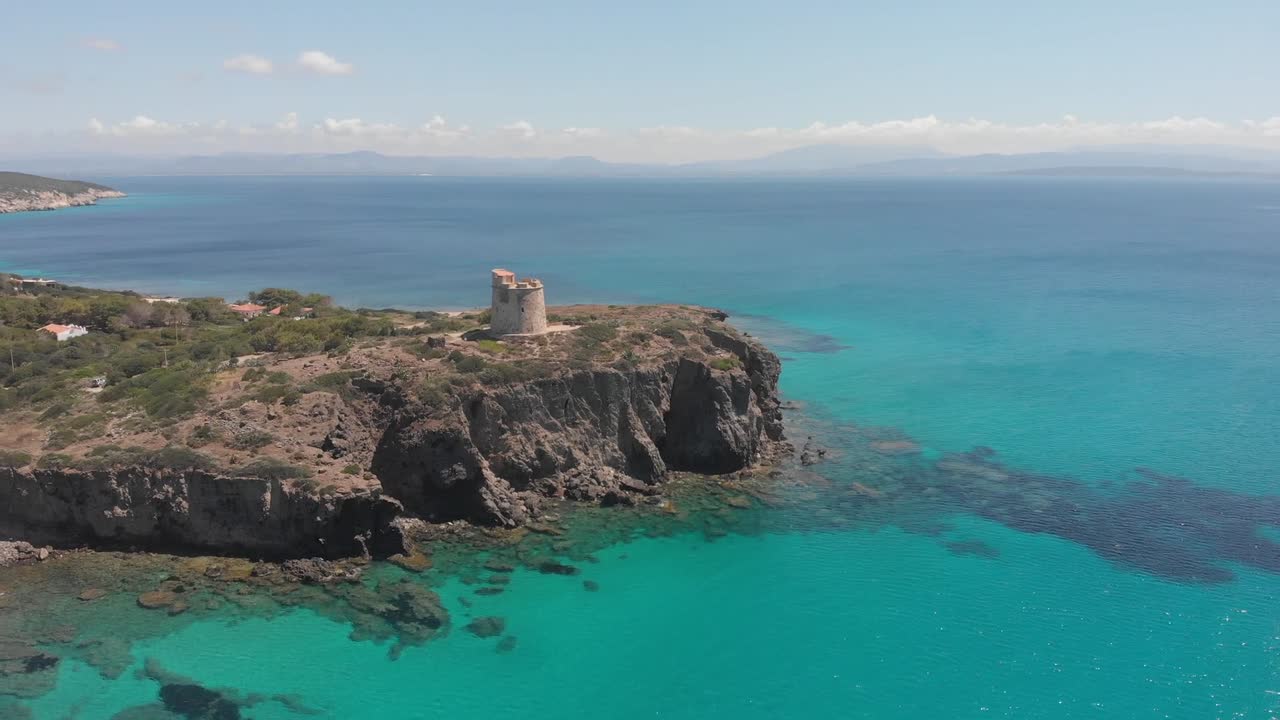 Ancient stone watchtower stands on rugged cliff above calm turquoise sea in Sardinia with clear skies and peaceful coastal scenery viewed from aerial perspective