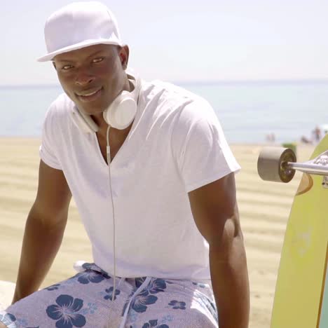 black skater next to his board and sandy beach