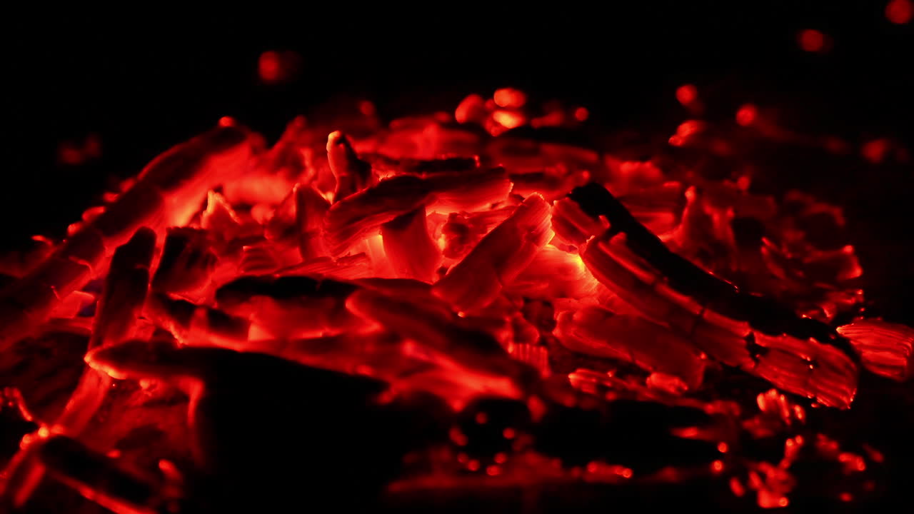 A pile of bright sparkling embers with some appearing flames. Close up view of burnt out bonfire.