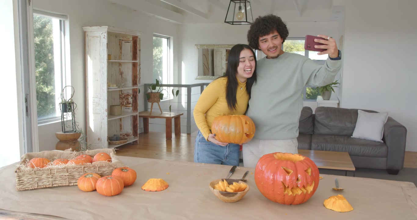 Coppia che scatta un selfie, posiziona una zucca, controlla il telefono e discute idee per intagliare zucche di Halloween a casa
