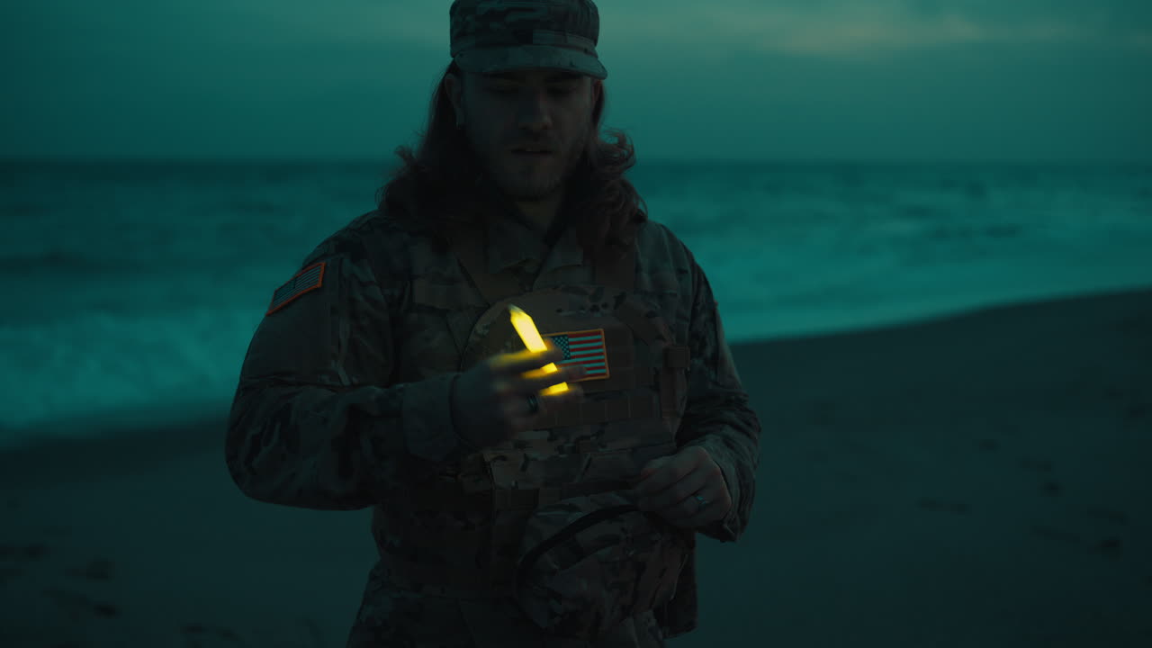 Silhuet af en amerikansk soldat tænder for en kemisk lygte for at overvåge en strand