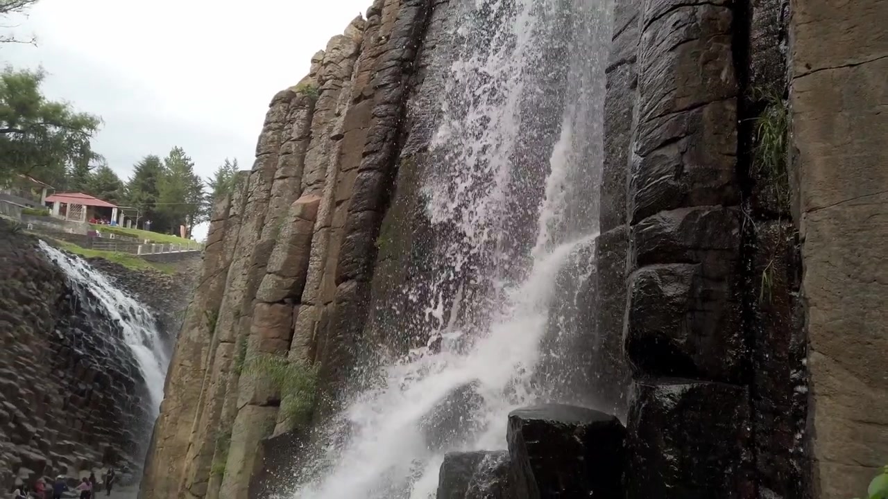 Foss som fosser ned ulendt fjellklippe med lagdelte steinformasjoner og rennende vann i Tizayuca, Mexico. Lav vinkel fremhever høyden på det steinete fossefallet.