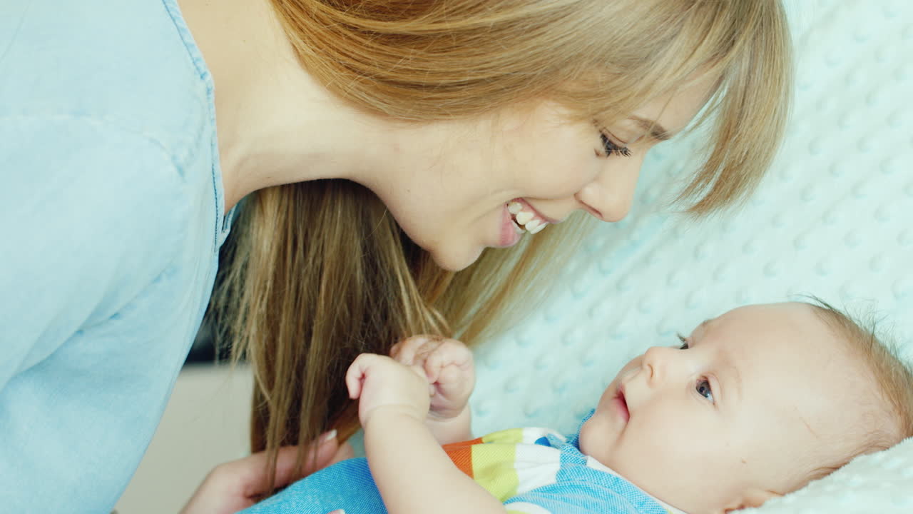 그의 펜을 들고 그녀의 아이 보고 행복 한 젊은 어머니 아기 침대에 누워