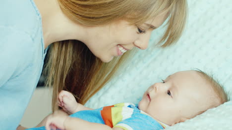 happy young mother looking at her child holding his pen the baby lies in the crib