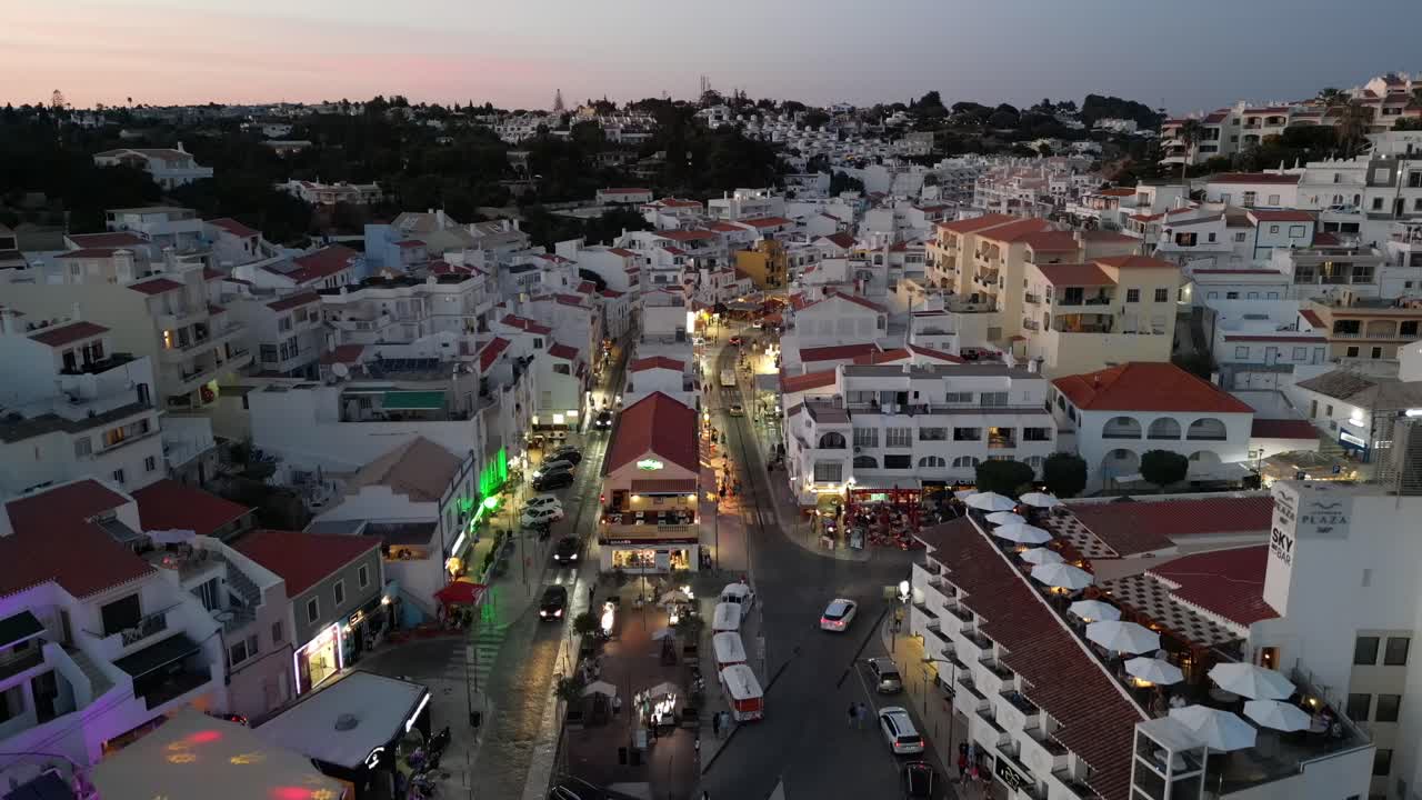 드론이 높은 고도에서 내려오면서 카메라가 카르보에이로의 주요 거리에 포르투갈 알가르베에서 해가 지면 불빛과 함께 사람들이 자동차와 레스토랑
