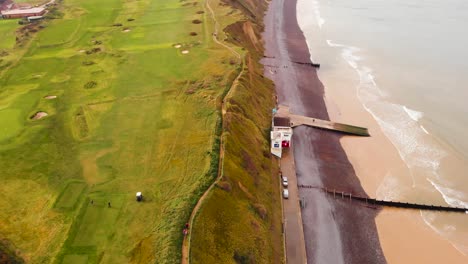 Aerial---Beach-and-seawall-on-North-Sea,-Sheringham,-England,-wide-forward-shot