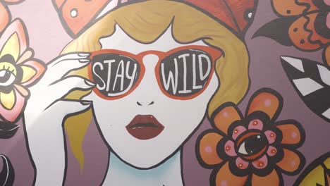 실내에서 햇빛이 비치는 "stay wild" 다채로운 벽화, 꽃 주위에 큰 모자를 쓴 여성 - 슬로우 모션 클로즈업