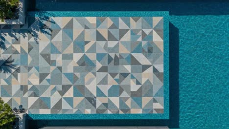aerial view of a beautifully designed geometric pool with blue water and artistic tile patterns highlighting a luxurious outdoor space