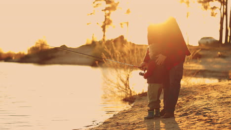 grandfather is teaching his grandson to fish on shore of lake in sunset happy family weekend