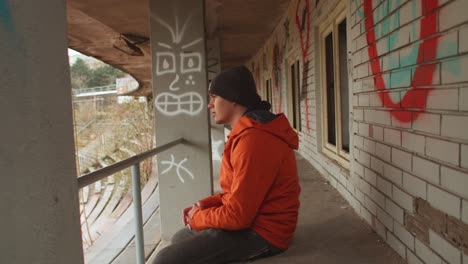 man in orange jacket gazes looking out to the side, pondering in abandoned urban stadium