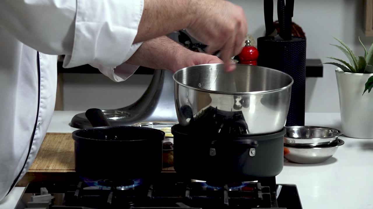 A chef skillfully prepares and measures ingredients in a well-equipped kitchen. The focus is on the stove, highlighting pots and attention to detail for a tasty dish