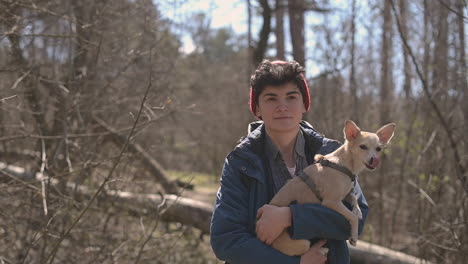 jovem fêmea com cabelo curto dá um passeio na floresta segurando um cachorro pequeno