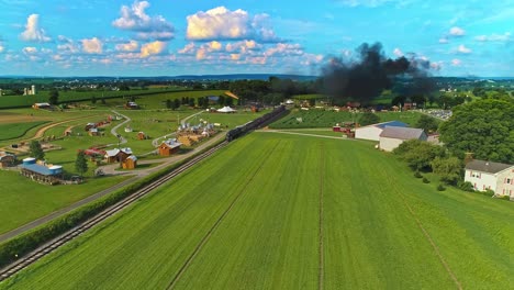 an aerial view of amish farm lands with a single rail road track and a steam passenger train approaching