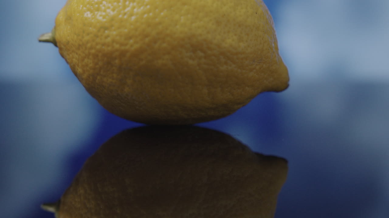 Il movimento della camera con inclinazione verso l'alto rivela un limone giallo che emerge dal suo riflesso mentre le nuvole passano sullo sfondo