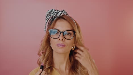 woman applying lipstick in front of pink background