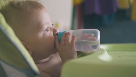 kid drinks water from bottle sitting in green highchair