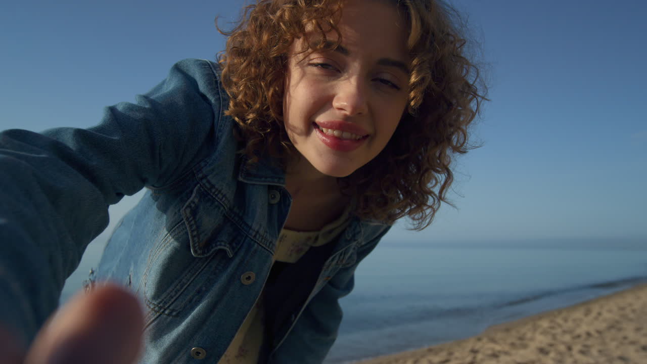 mujer feliz sonriendo encendiendo la cámara en la playa de cerca. chica rizada agitando las manos
