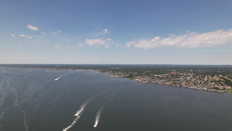 Ein-Blick-Aus-Der-Vogelperspektive-Auf-Die-Große-Südbucht,-Während-Unten-An-Einem-Wunderschönen-Tag-Mit-Blauem-Himmel-Und-Weißen-Wolken-Vier-Boote-Um-Die-Wette-Rasen