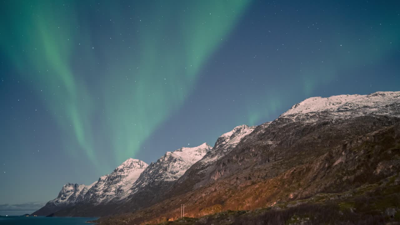 una exhibición de aurora boreal iluminada por la luna sobre los fiordos árticos y las montañas del norte de noruega