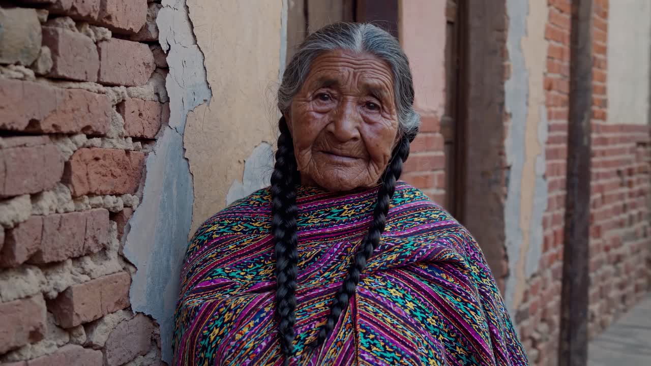 Portrait of a serene indigenous elder posing against a weathered brick wall, her long braided hair and vibrant shawl reflecting her cultural heritage