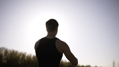 the athlete trains in nature. the spring sun is shining. do exercises with weight. backside from below footage