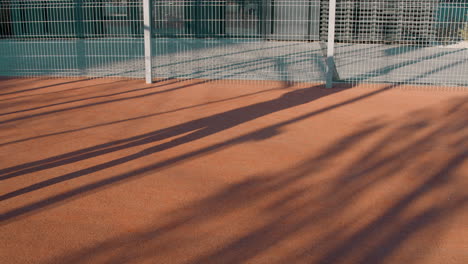sombras de personas proyectadas en una superficie al aire libre junto a una valla metálica