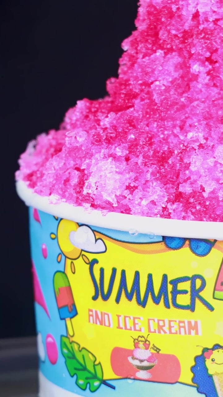 Granita rosa brillante in una tazza colorata con grafiche estive giocose, ripresa in un ambiente ben illuminato.