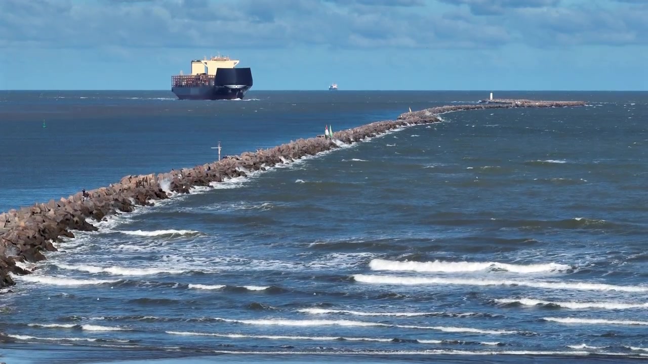 Vista aerea ascendente del frangiflutti e della nave da carico che entra nel canale di navigazione a Rio Grande, Brasile.