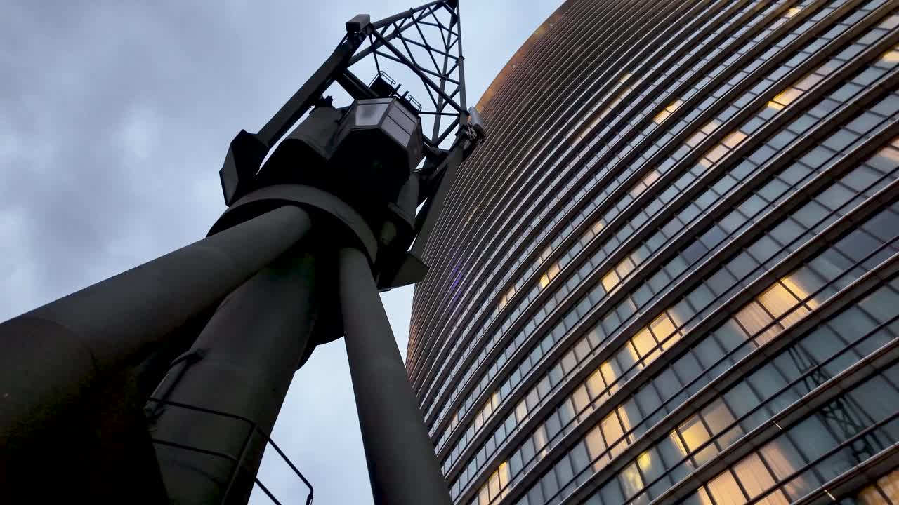 Tall building with illuminated windows and an old modern crane in foreground at Canary Wharf