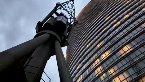 tall building with illuminated windows and an old modern crane in foreground at canary wharf