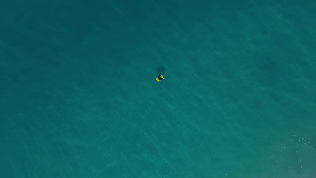 Bodyboarder alone in ocean waiting on waves, top down drone view