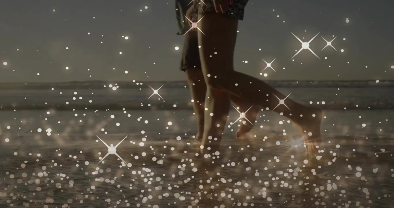 Coppia che passeggia tra le onde, le gambe che entrano da destra creando spruzzi e lasciando impronte.