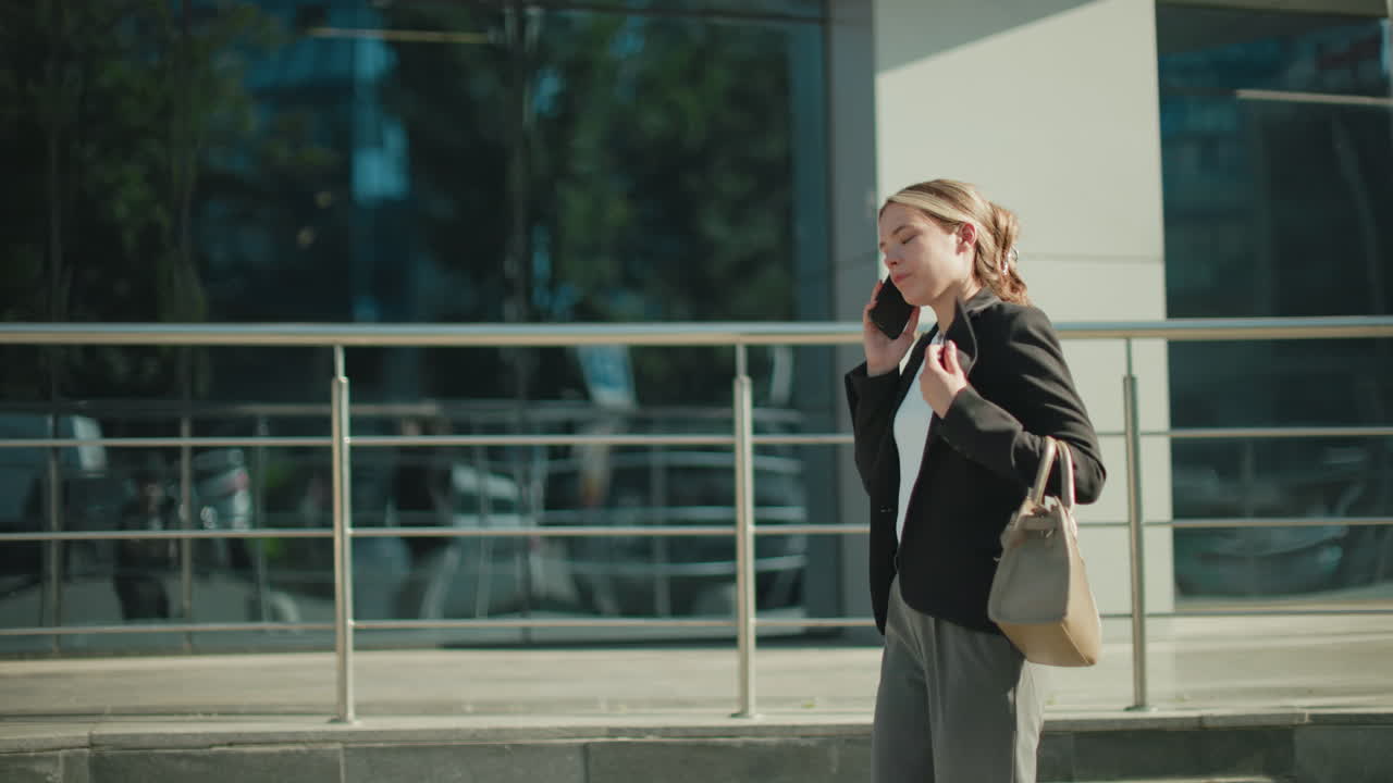 Side view of young banker on phone with customer visibly frustrated, raising hands in anger while walking past mall with modern glass facade reflecting street and urban background