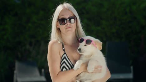 A-woman-in-a-bikini-holds-a-blonde-puppy-in-sunglasses-in-her-arms.-Summer-and-vacation-with-a-pet-concept