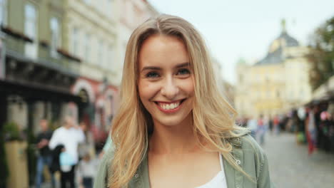 close-up view of caucasian blonde woman looking straight to the camera while taking a photo in the street