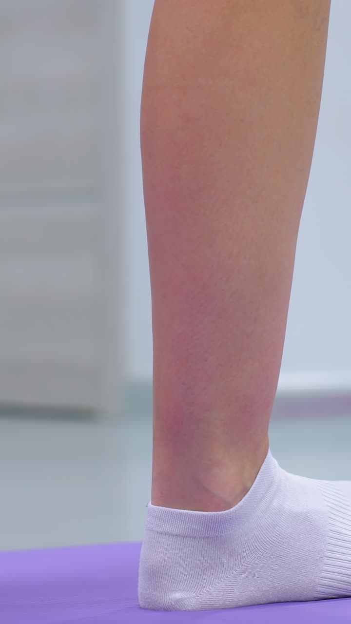 vista lateral de la pierna de una mujer con calcetines ajustando su pierna hacia atrás en una alfombra púrpura para el equilibrio durante una sesión de fitness, centrándose en la postura y la posición de las piernas