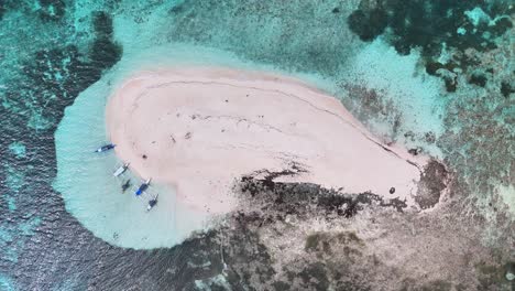 drone view of a small sandbar in the siargao islands, philippines, surrounded by shallow turquoise water and coral reefs, with several traditional boats anchored along the sandy shore during low tide