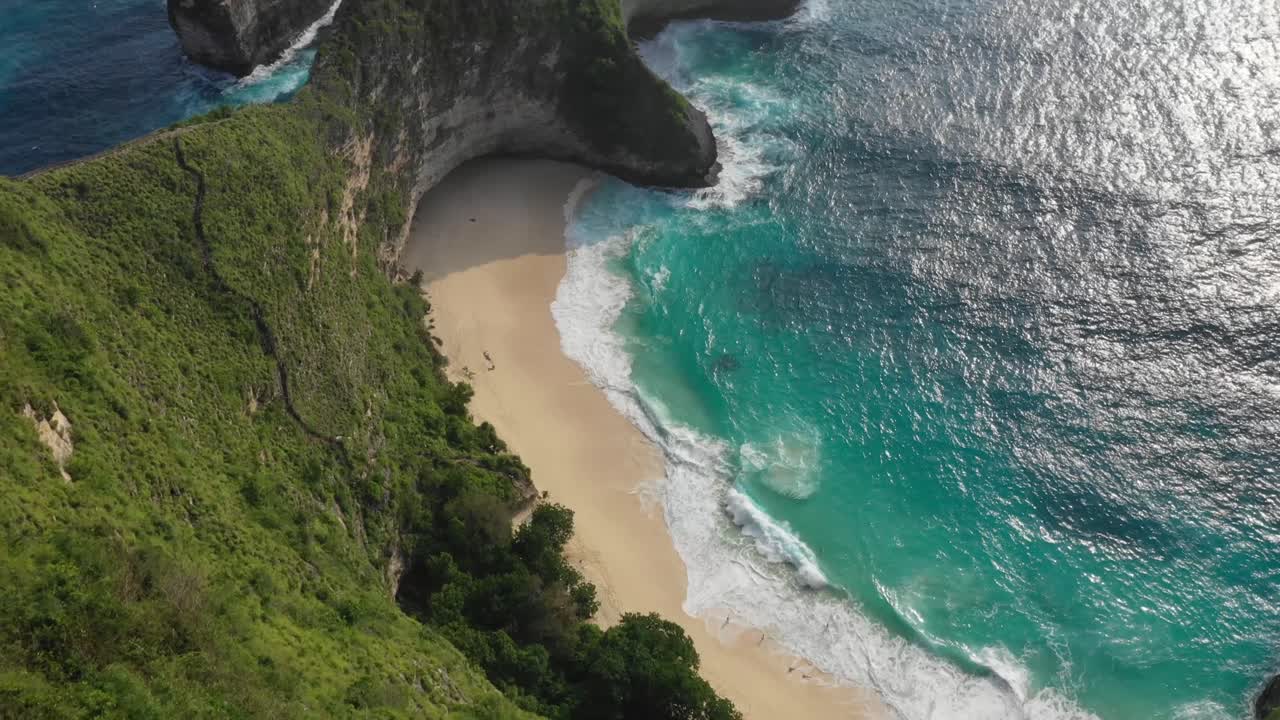 Ripresa aerea dall'alto con un uomo sul bordo della scogliera che rivela una spiaggia tropicale