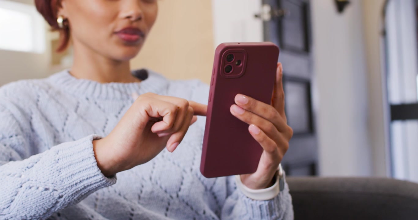 Donna afroamericana che tiene uno smartphone, tocca e scorre lo schermo sul divano, con il microfono che rimane agganciato.