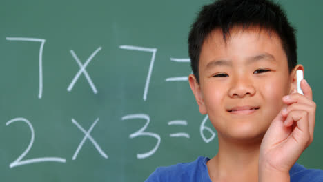 front view of asian schoolboy standing against chalkboard and showing chalk in classroom 4k