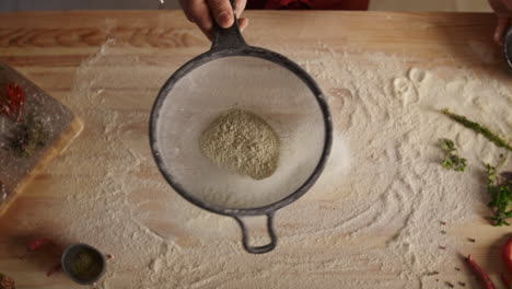 baker cooking sifting flour on wooden cutting board in pizza restaurant kitchen.