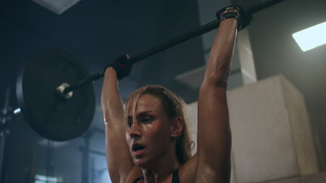a female weightlifter performs a barbell lift in a dark gym. a woman lifting a heavy bar over her head