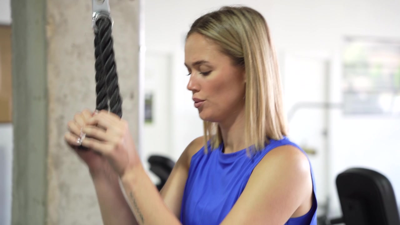 Una donna dimostra dedizione eseguendo estensioni per tricipiti ai cavi in palestra.