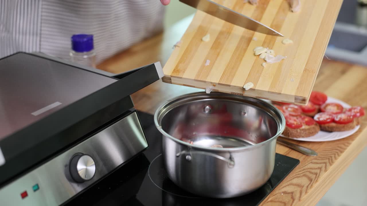 Chef's Hands Transferring Chopped Garlic from Cutting Board to Pot