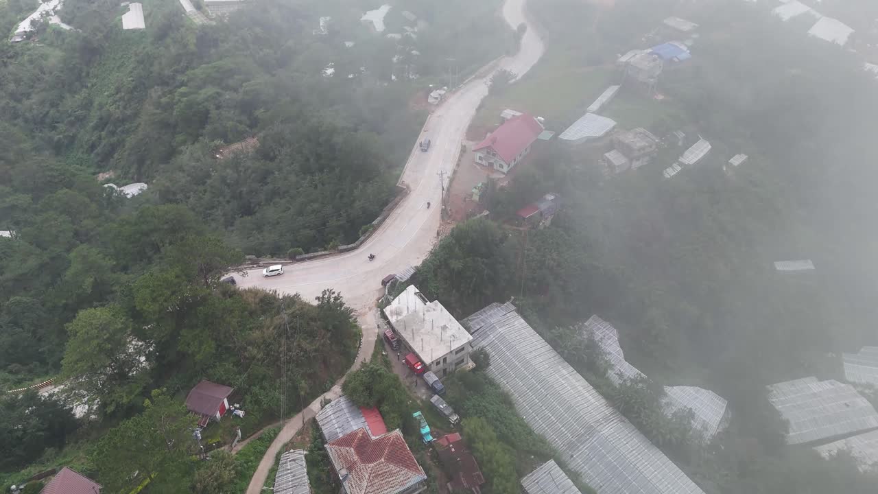 Aerial view of a misty mountain road and rural landscape with greenhouses
