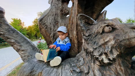 little boy sitting on the cat statue carved from wood. cute toddler is focused on the book.