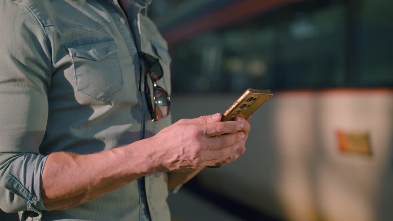 Stylish solo male traveler checking phone and swiping at Seoul train station in Korea, urban setting with strong sunlight