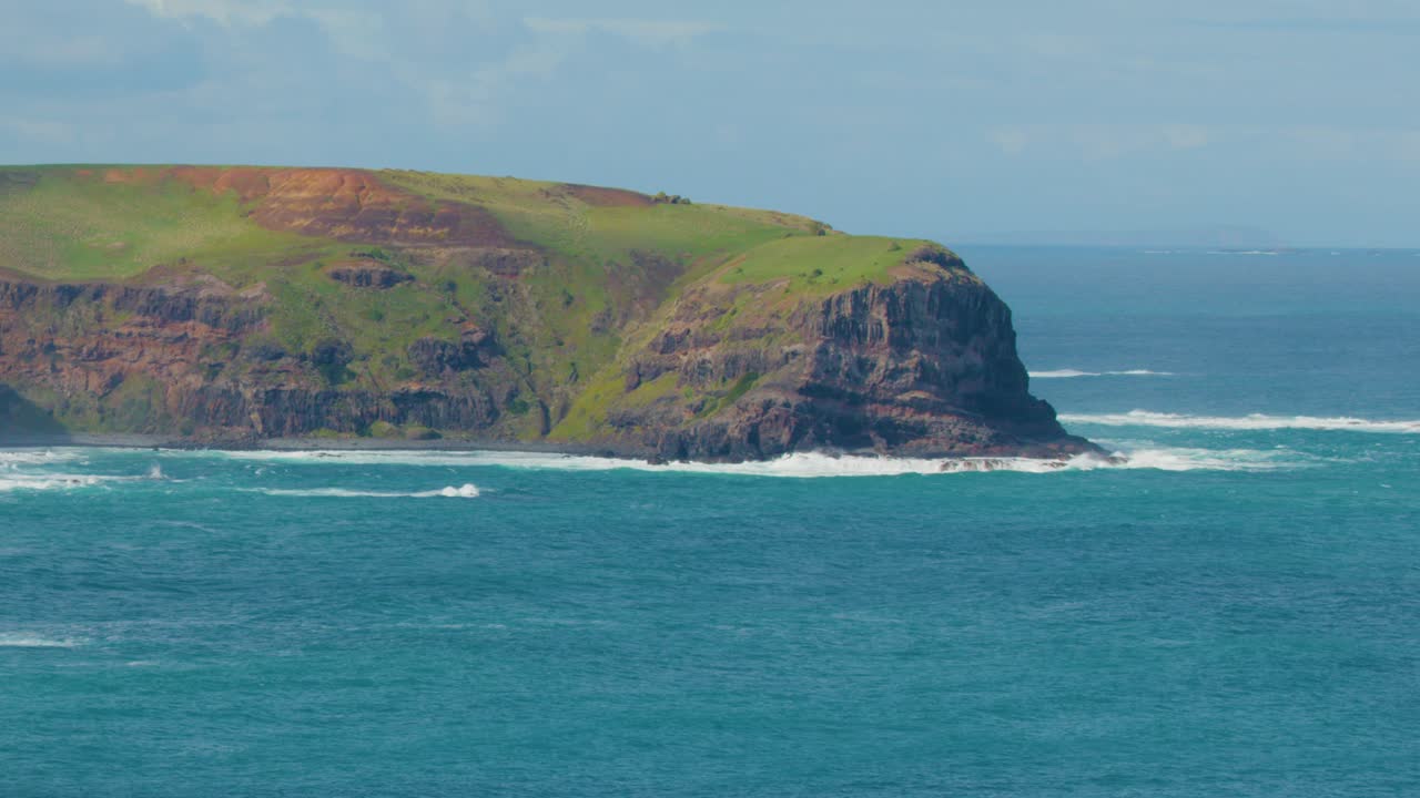 Wide daytime pan across grassy cliffs, rocky coastline, and turquoise ocean under bright natural light